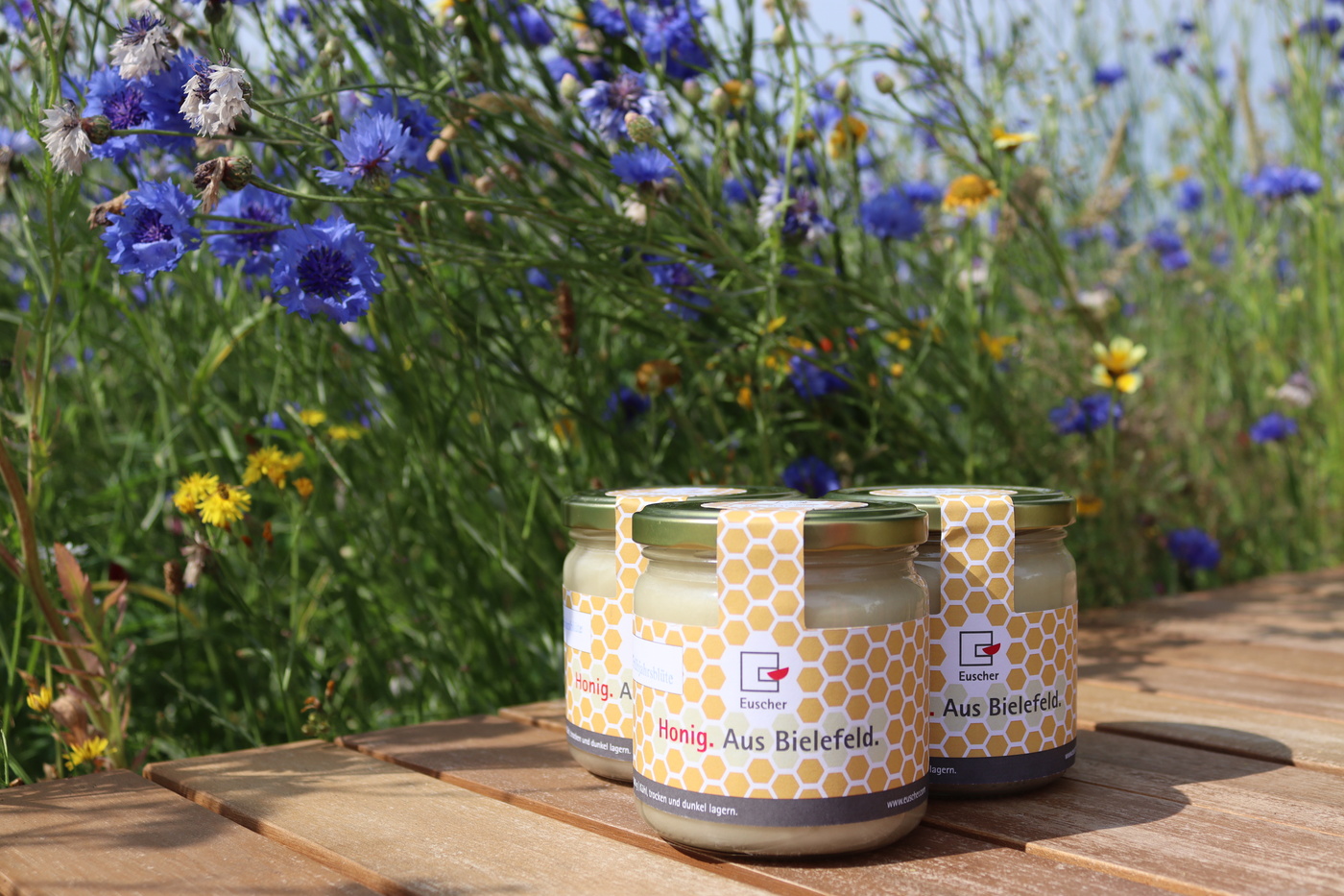 Das Bild zeigt einen Blumenwiese und davor den eigenen Honig der Euscher GmbH & Co. KG