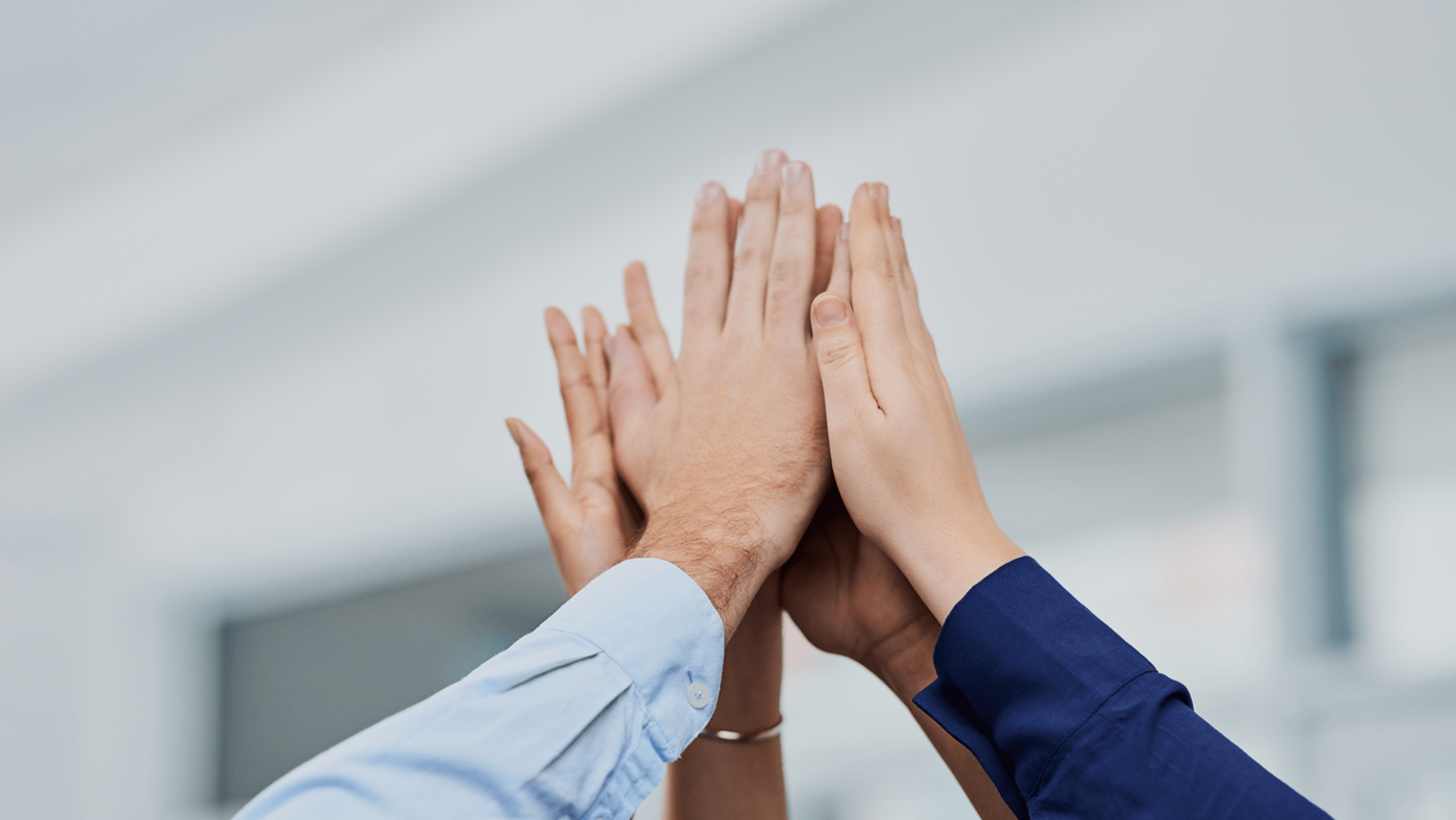 Die Hände einer Gruppe verschiedener Menschen schlagen zum High Five zusammen.