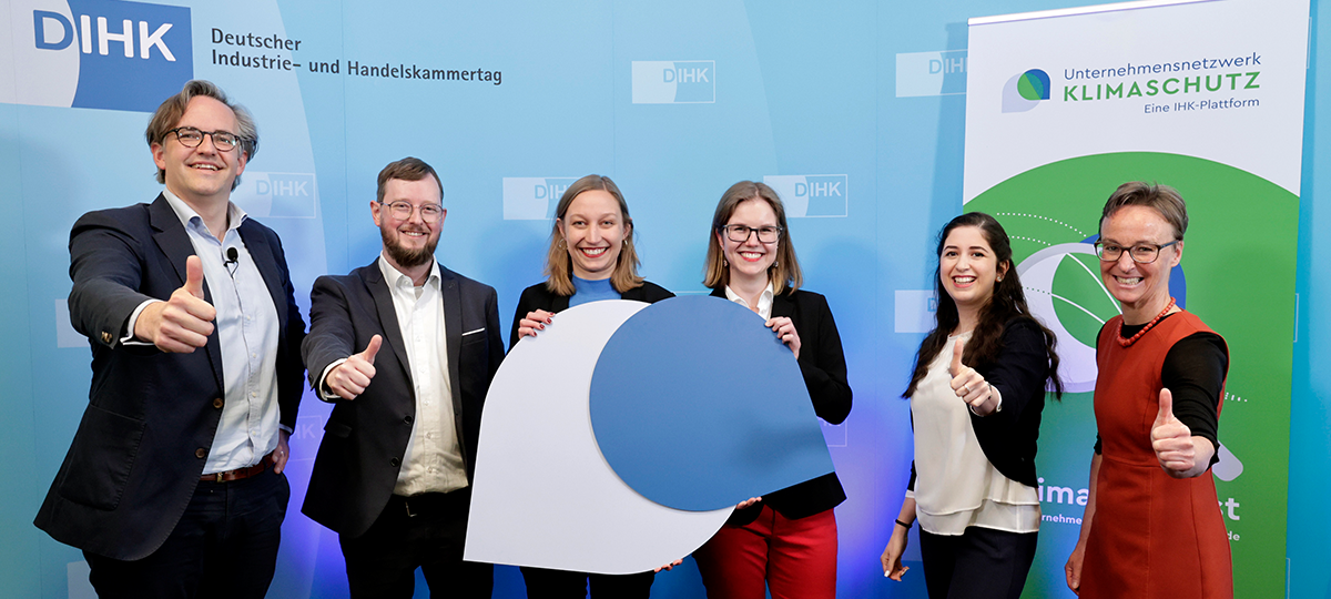 Das Bild zeigt die Teammitglieder des Unternehmensnetzwerks Klimaschutz und die Geschäftsführerin der DIHK Service GmbH. Die Personen in der Mitte halten das UNK-Logo aus zwei Hälften zusammen, während die übrigen Personen ihre Daumen in die Kamera recken.
